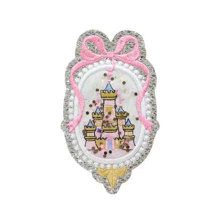 Princess castle shaker embroidery patch featuring a glitter silver scalloped frame, pink bow detail, and embroidered fairy tale castle with loose sparkle confetti inside. This handmade princess castle appliqué patch is shown isolated on a white background and is designed for kids clothing, dresses, backpacks, jackets, and craft projects.