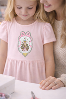 Princess castle embroidery patch centered on a light pink girls dress, showcasing a fairytale castle design with pink bow, glitter accents, and detailed embroidery. This princess castle patch is ideal for kids dresses, shirts, jackets, and handmade sewing projects.