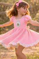 Princess castle shaker embroidery patch sewn onto a pink girls dress, featuring a glitter silver scalloped frame, pink bow detail, and embroidered fairytale castle with loose sparkle confetti inside. This handmade princess castle sew on patch is shown worn on children’s clothing to demonstrate use on dresses, outfits, and special occasion apparel.
