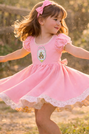 Princess castle shaker embroidery patch sewn onto a pink girls dress, featuring a glitter silver scalloped frame, pink bow detail, and embroidered fairytale castle with loose sparkle confetti inside. This handmade princess castle sew on patch is shown worn on children’s clothing to demonstrate use on dresses, outfits, and special occasion apparel.