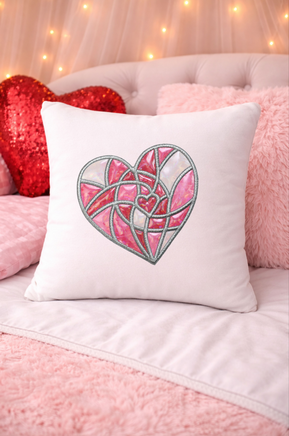 Decorative pillow with a heart design on a pink couch with a heart-shaped pillow and fairy lights in the background.
