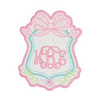 Floral bow crest monogram embroidered patch with scalloped pink border, aqua frame detail, delicate flowers and greenery, and custom script initials, perfect for personalized jackets, backpacks, dresses, and boutique accessories