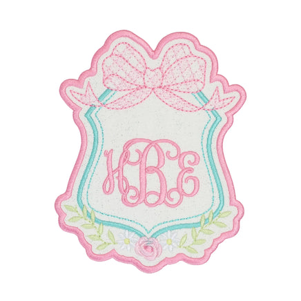 Floral bow crest monogram embroidered patch with scalloped pink border, aqua frame detail, delicate flowers and greenery, and custom script initials, perfect for personalized jackets, backpacks, dresses, and boutique accessories