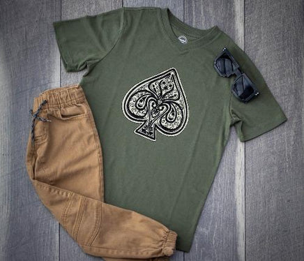 Ace of spades embroidery patch sewn onto a green t-shirt, featuring an ornate black and white spade design with intricate scroll work and satin stitched edges. This decorative ace of spades sew on patch is shown styled on casual clothing to demonstrate use on shirts, jackets, denim, backpacks, and handmade sewing projects.